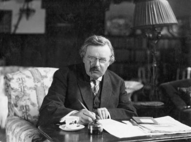 Portrait photograph of G.K. Chesterton sitting at desk.